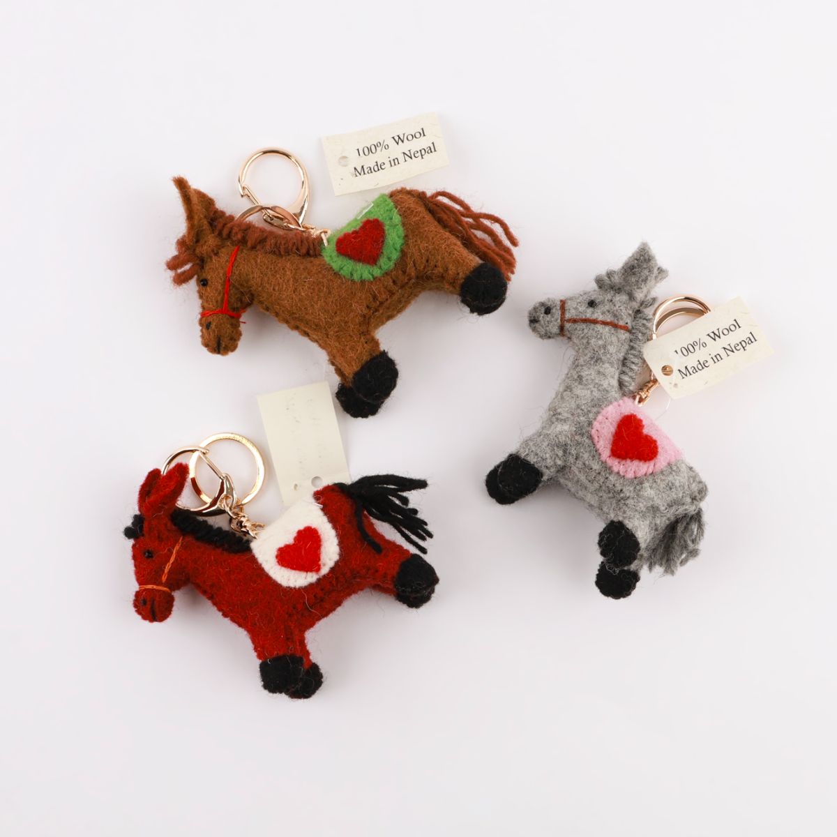 Three handmade felt horse keychains with Nepal tags flat lay on white background