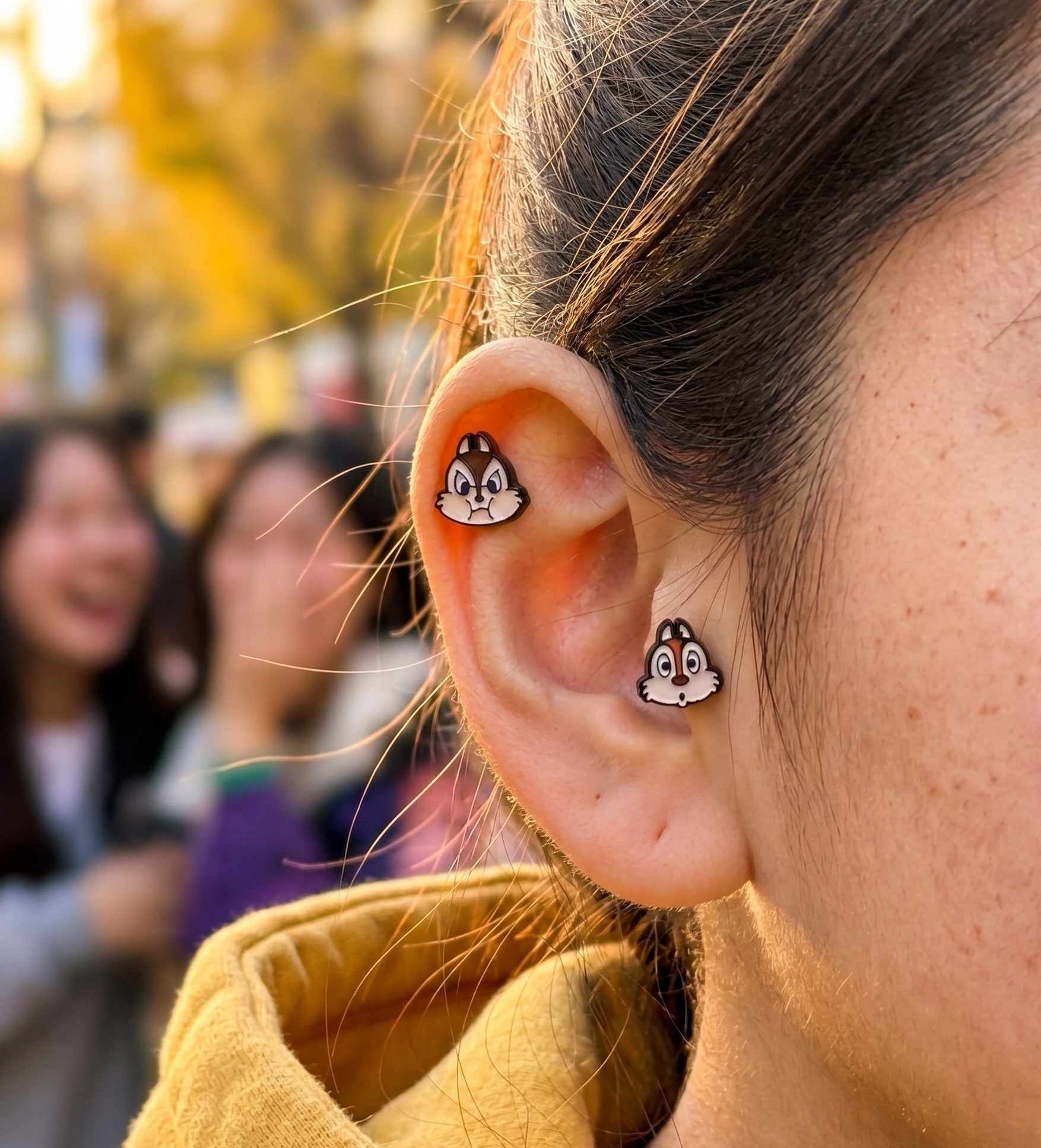 Chip and Dale enamel piercing studs in natural daylight — inner helix and lobe placement, vibrant enamel color detail, Disney licensed jewelry