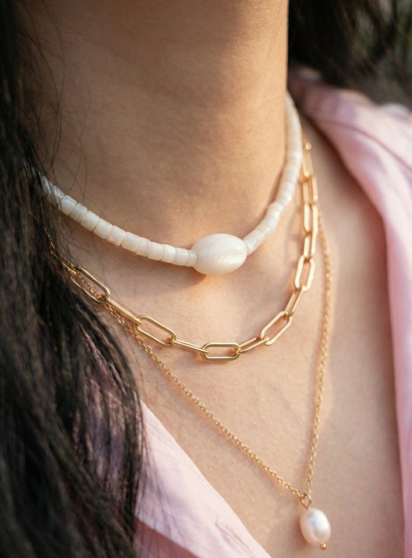 Close-up of white heishi bead choker on collarbone with gold layered necklaces