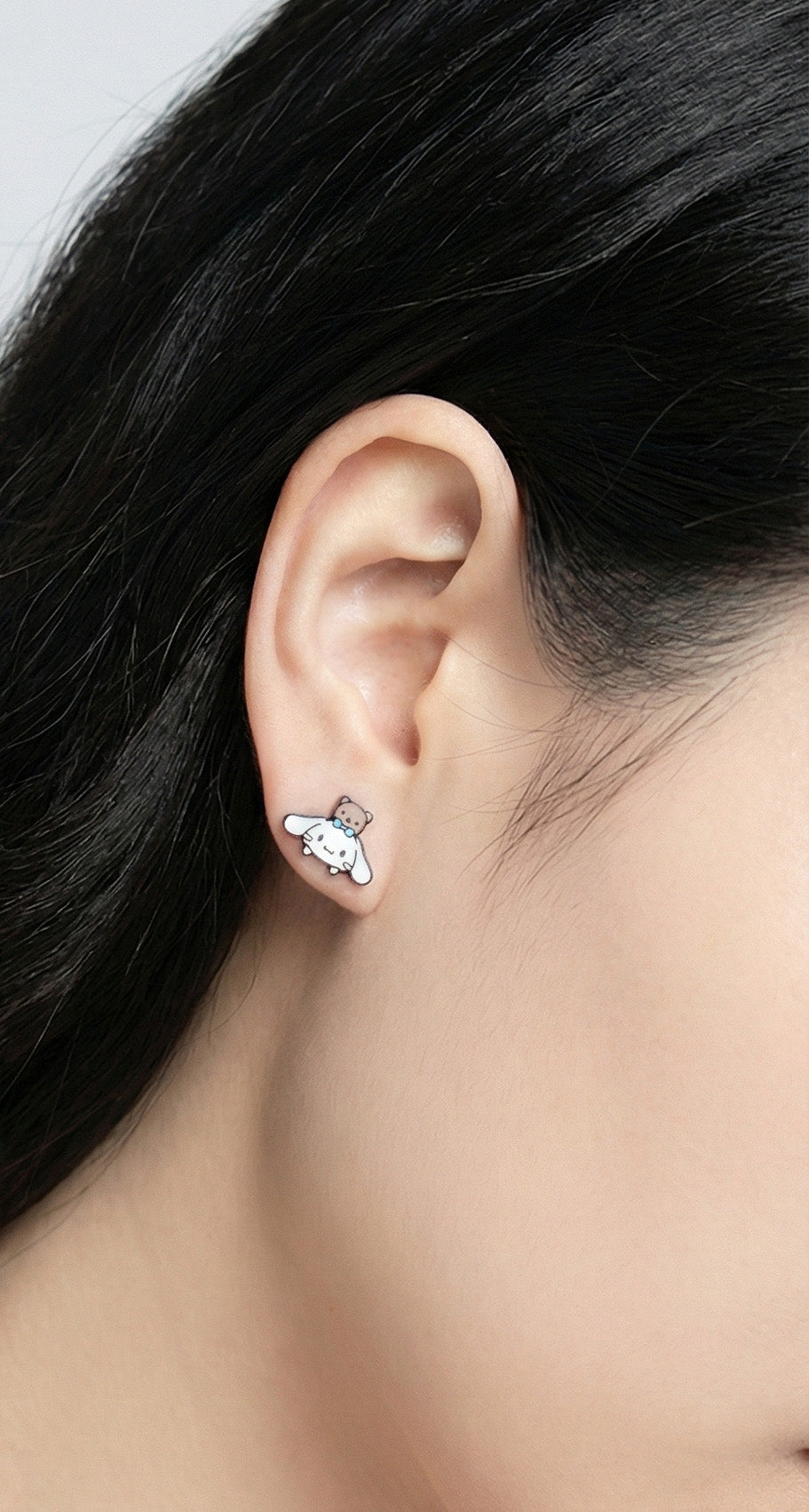 Side view of white puppy and bear character earring on ear showing asymmetric placement