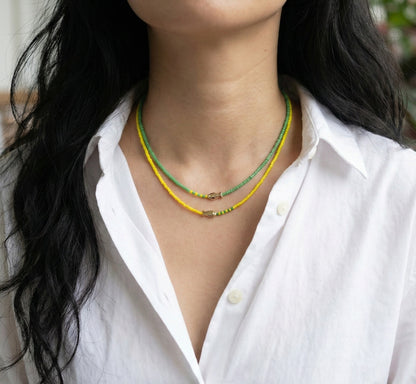 Green and yellow seed bead fish necklaces layered on woman with white shirt fresh spring style