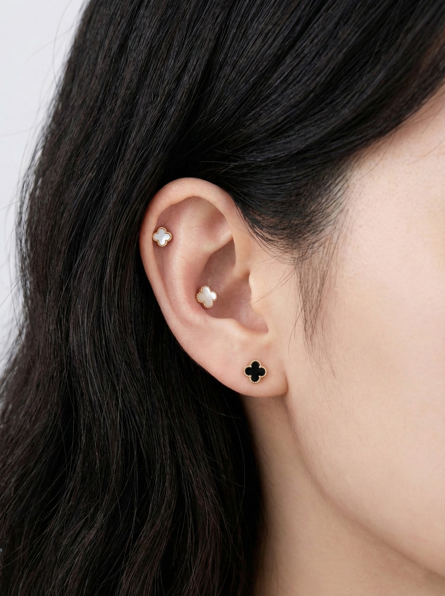 Woman wearing white and black mother of pearl clover piercings with titanium posts in cartilage helix conch and lobe ear styling