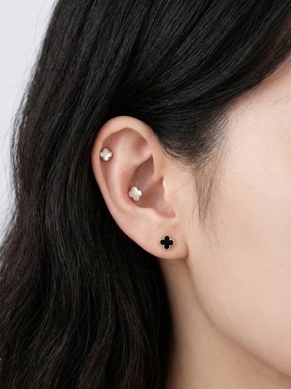 Woman wearing white and black mother of pearl clover piercings with titanium posts in cartilage helix conch and lobe ear styling