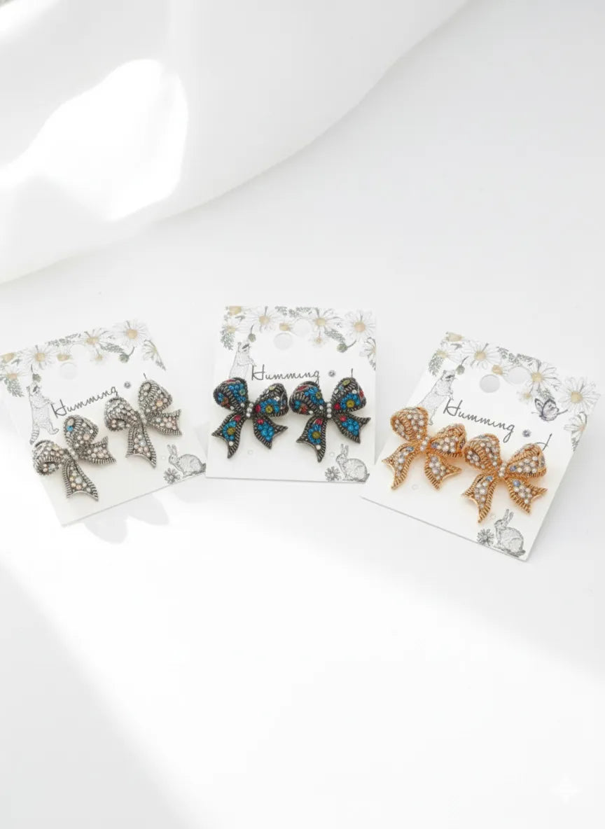 Three colorways of crystal bow stud earrings on jewelry cards — Antique Multi (dark with multicolor crystals), Silver Blue (antique silver with blue crystals), and Gold Pink (gold with pink crystals) — handmade in Korea