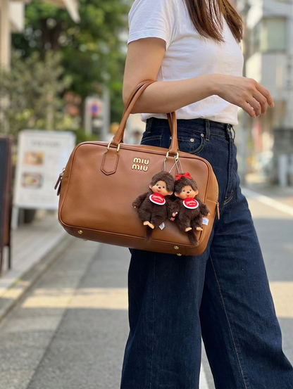 Monchhichi Classic Boy and Ribbon Girl plush keychains paired together on tan Miu Miu bowling bag — couple matching bag charms