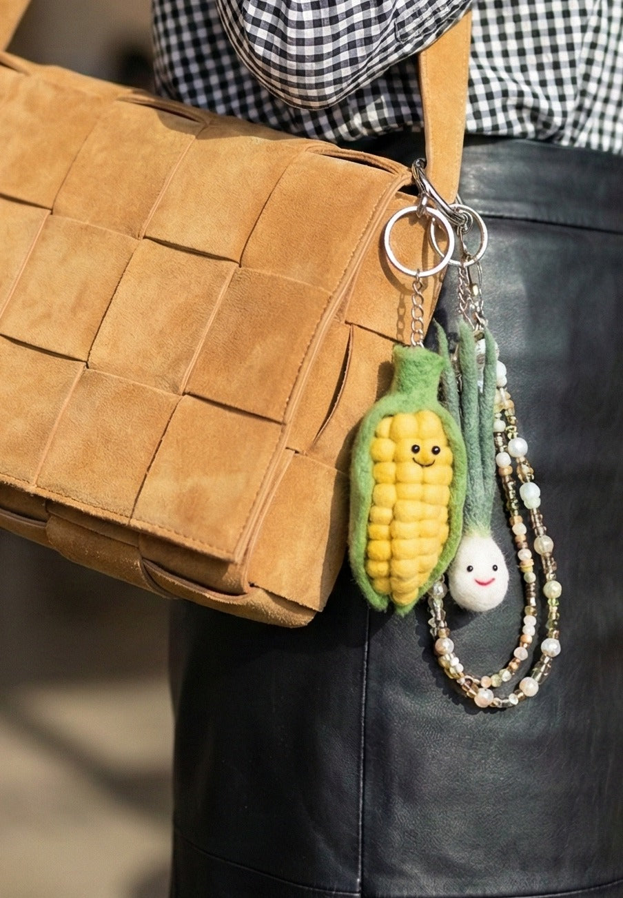 Gingham shirt and leather bag accessorized with corn and scallion keychains plus pearl chain