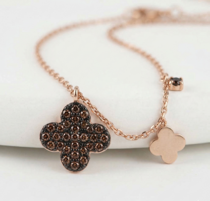 Close-up of cognac brown pavé clover necklace on décolletage – rose gold chain with mini clover charm and black cubic charm detail