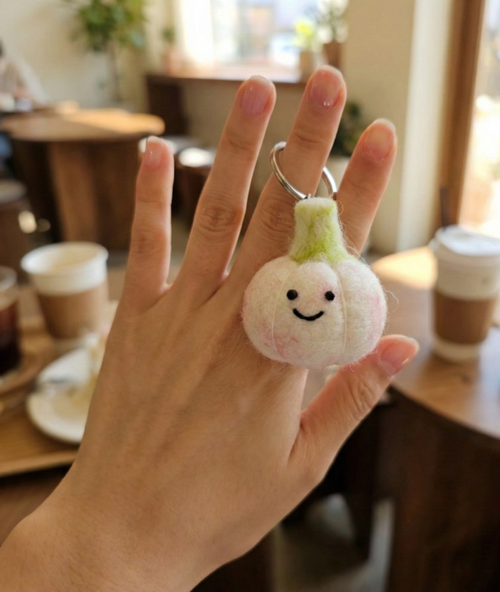 Hand holding white garlic felt keychain at coffee shop