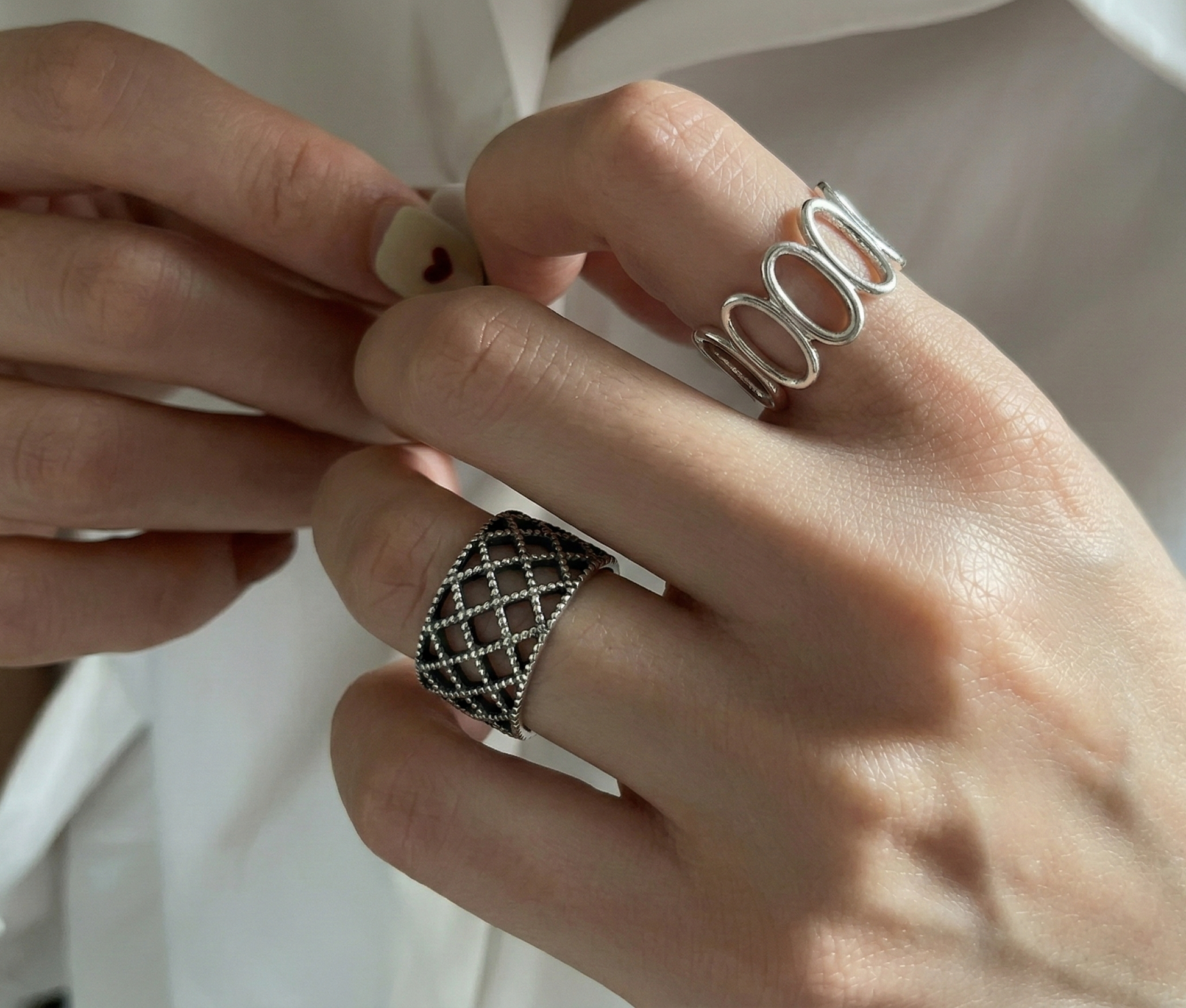 Both sterling silver rings worn on both hands — lace lattice on lower finger, oval loop on upper finger, white shirt background, layered ring styling