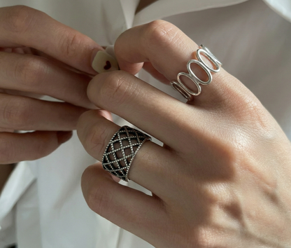 Both sterling silver rings worn on both hands — lace lattice on lower finger, oval loop on upper finger, white shirt background, layered ring styling