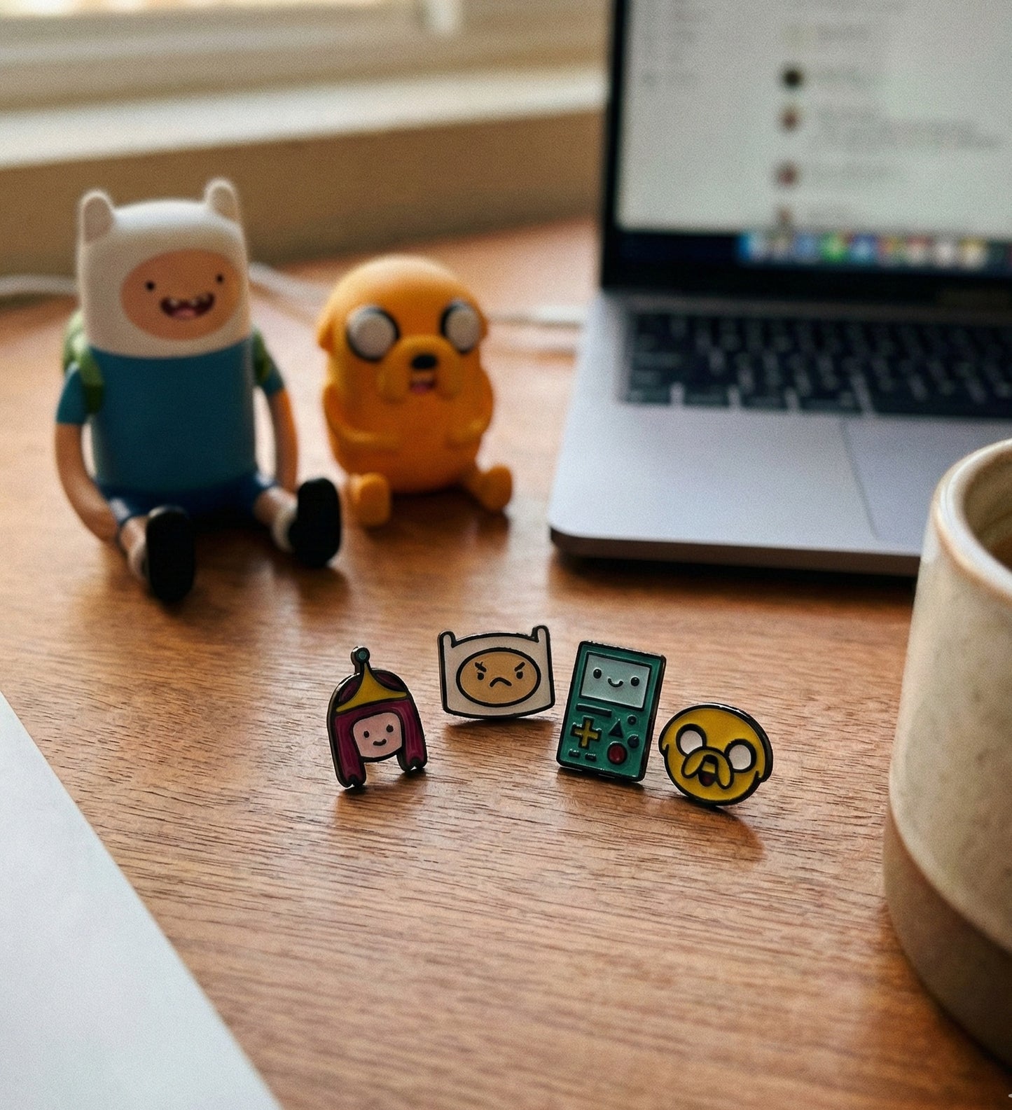 Lifestyle flat lay Adventure Time earrings on desk with Finn and Jake figurines laptop and coffee mug
