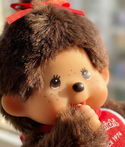 Extreme close-up of Monchhichi Ribbon Girl face showing hand-painted freckles, shimmering eyes, and red satin bow — premium detail shot