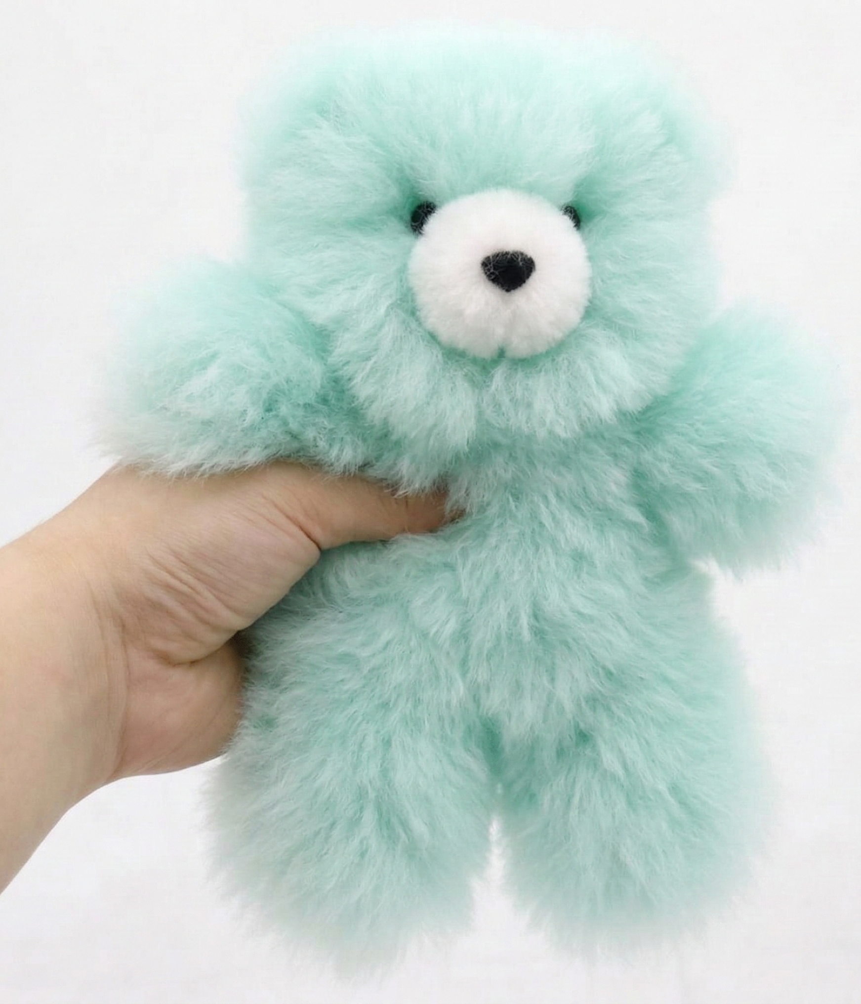 Light blue plush toy held by a hand on a white background