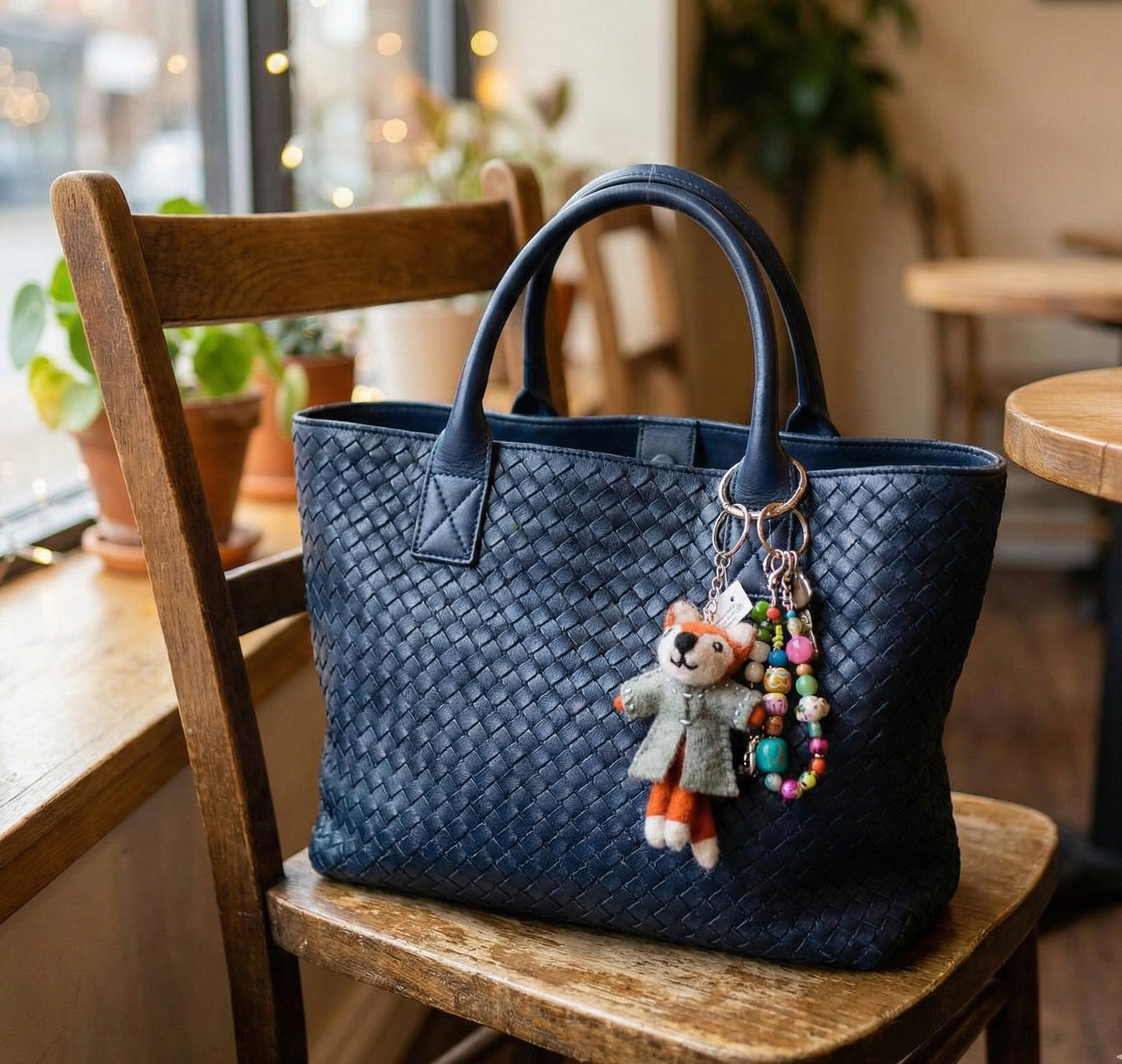 Navy woven tote bag with wool felt raccoon and colorful bead keychains in cafe