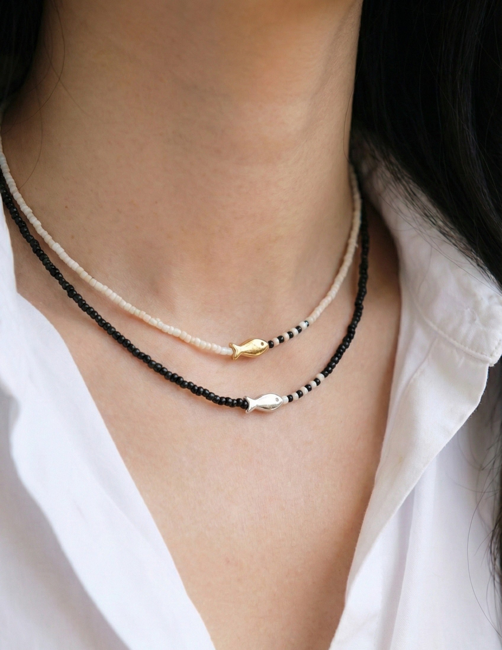 Detail of black and ivory beaded necklaces with gold and silver fish charms elegant layering
