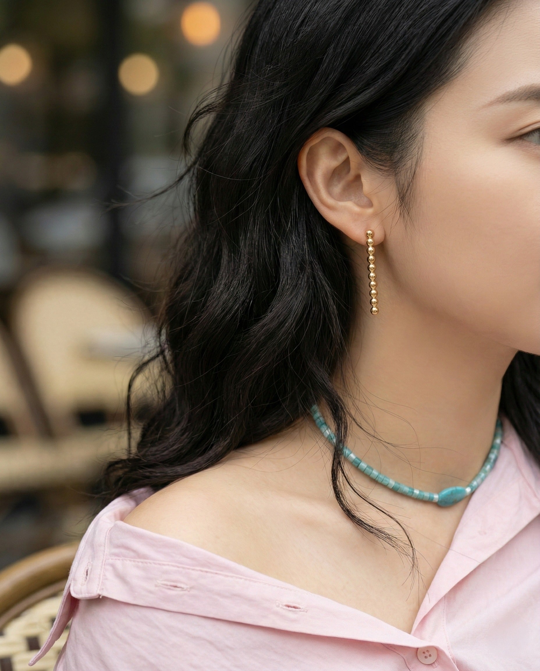 Woman wearing gold ball drop earrings with pink shirt and turquoise necklace - lifestyle shot