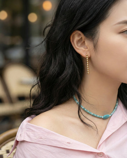 Woman wearing gold ball drop earrings with pink shirt and turquoise necklace - lifestyle shot