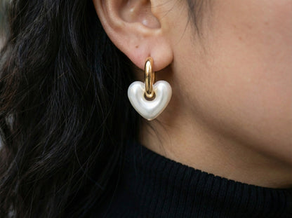 Woman wearing pearl white heart huggie earrings with black turtleneck, side profile ear shot