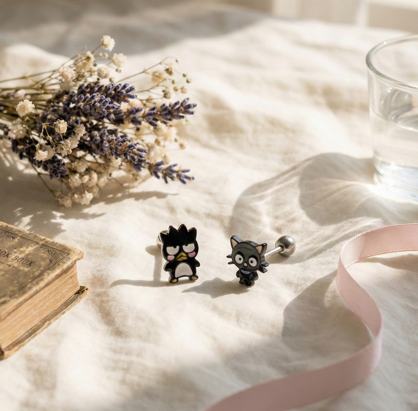 Flat lay of Badtz-Maru and Chococat surgical steel studs with lavender flowers and vintage book