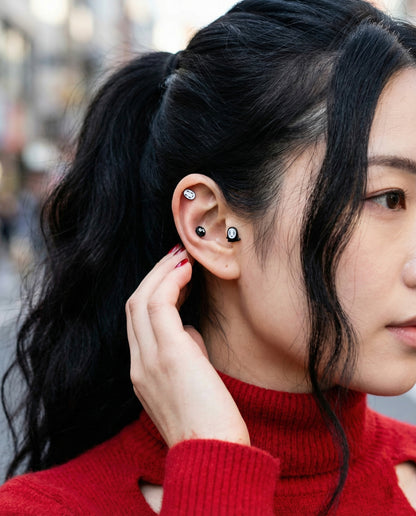 Profile and close-up shots of model wearing Ghibli-themed ear stack featuring No-Face studs in various placements, red nail polish matching red sweater, Studio Ghibli fashion accessories inspiration.