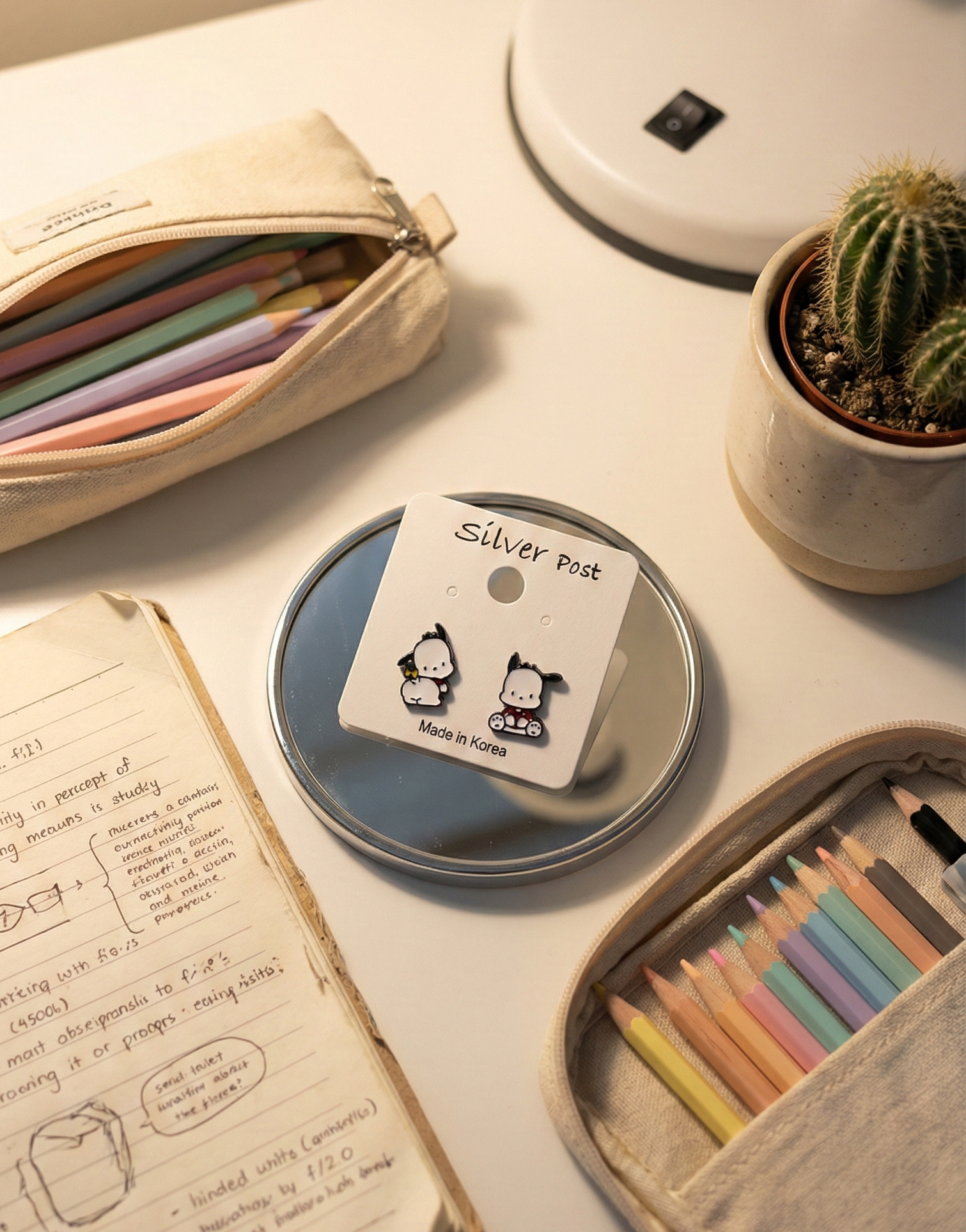  Pochacco earrings on silver post card next to study desk with colorful pens and cactus plant
