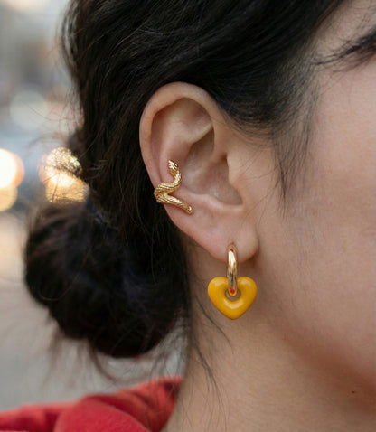 Side view of woman wearing mustard yellow puffy heart earrings with white shirt, clean background