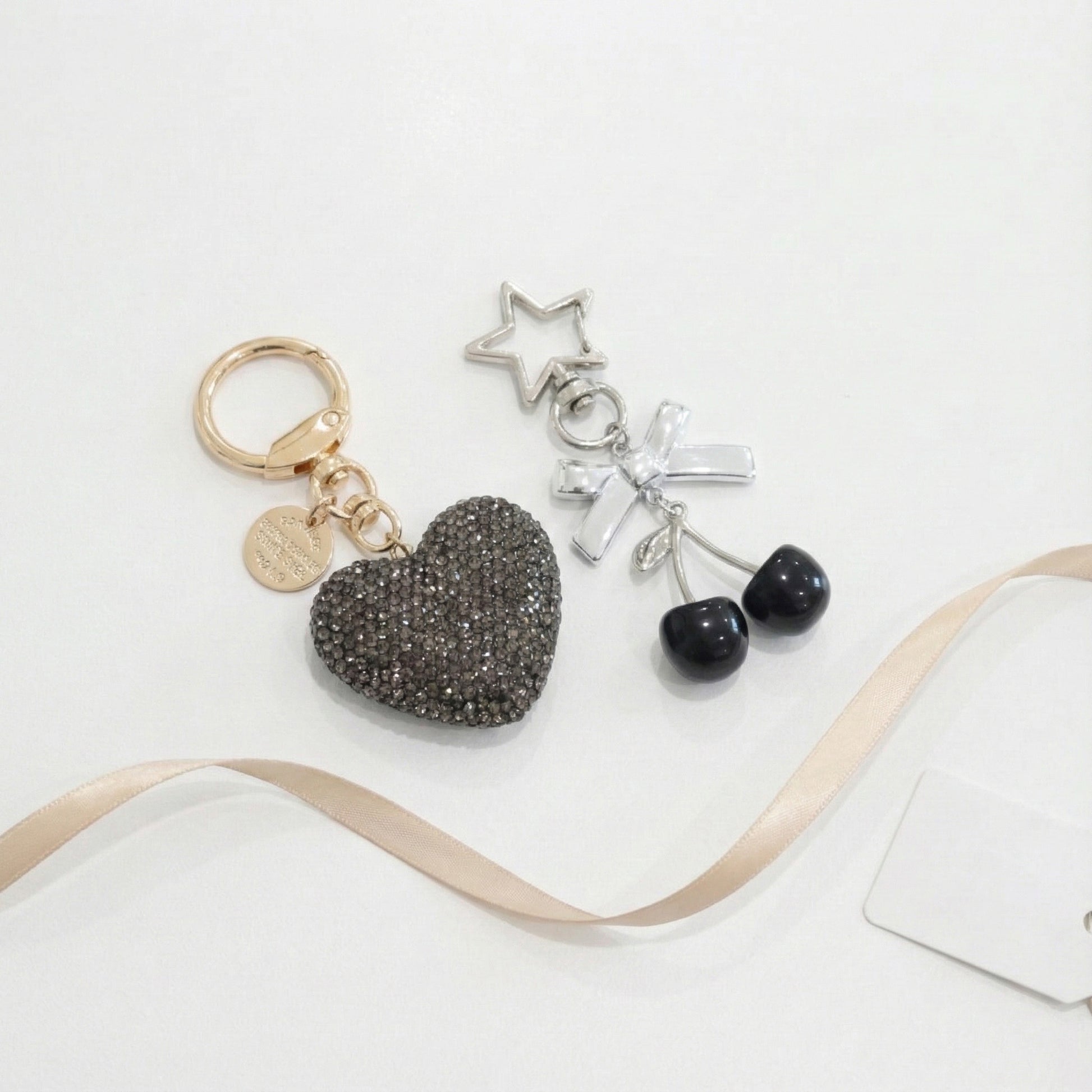 Black rhinestone heart and black cherry charm keychain with silver bow and star, styled with beige ribbon