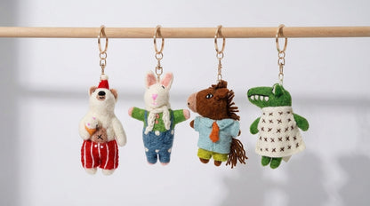 Four plush keychains shaped like animals hanging on a rod against a light background