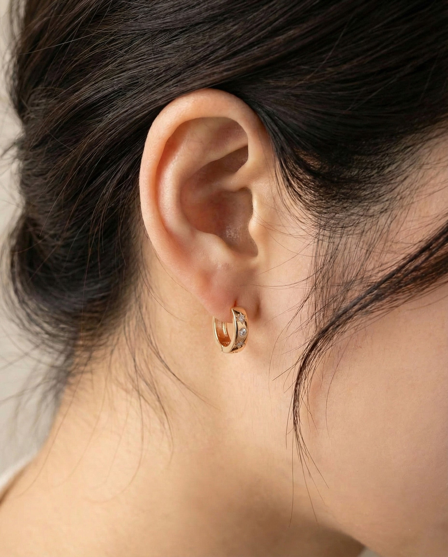 Close-up of a rose gold hoop earring with cubic zirconia stars worn on the left ear, side profile view.