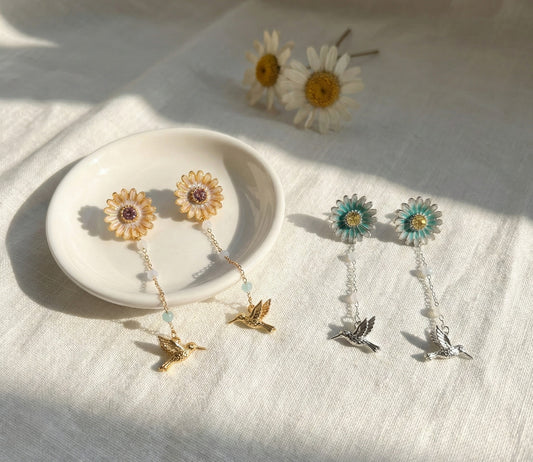 Handmade daisy flower and hummingbird front-back drop earrings in gold and silver on white plate