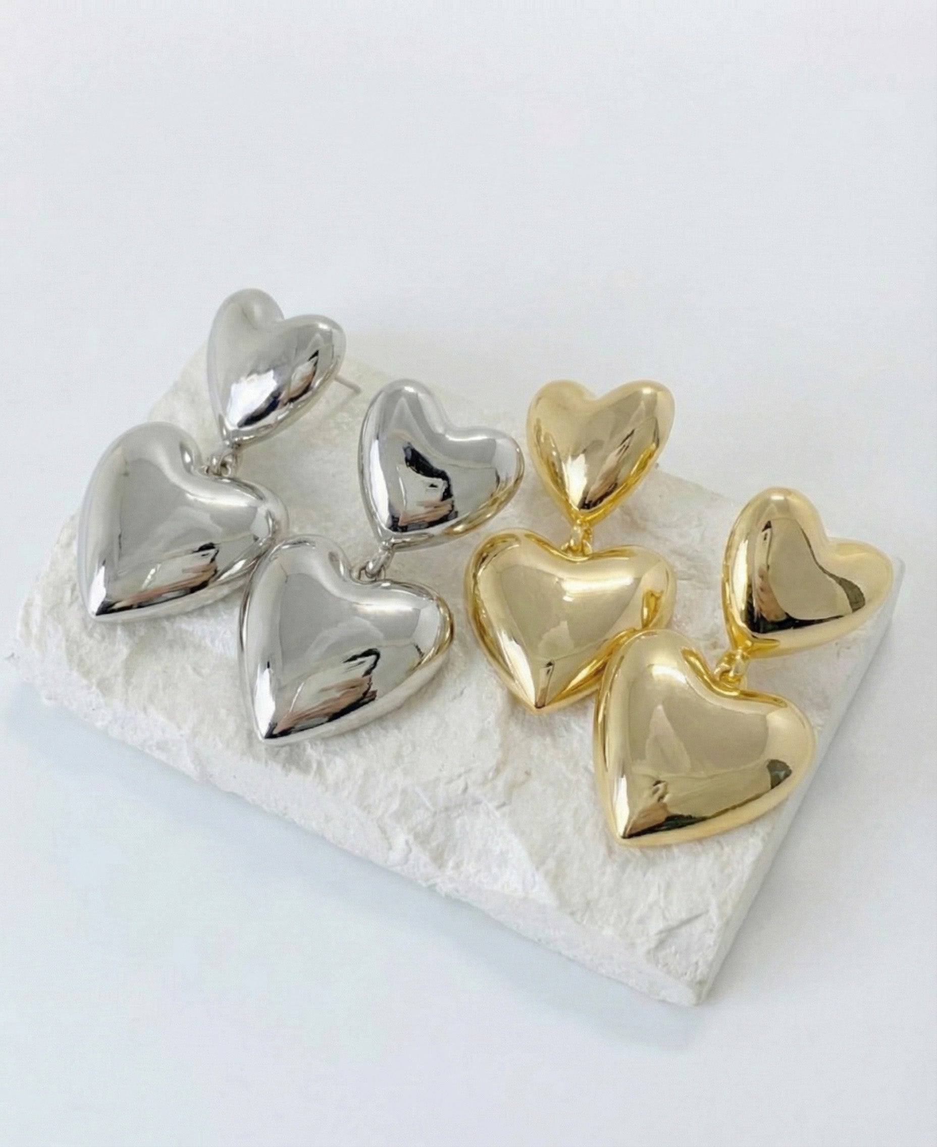 Chunky puffed double heart drop earrings in gold and silver on white stone display