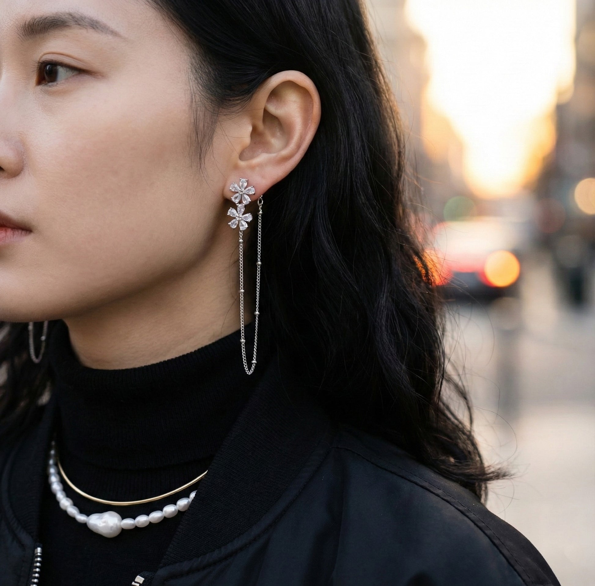 Woman wearing silver floral crystal chain drop earrings with black turtleneck outdoors