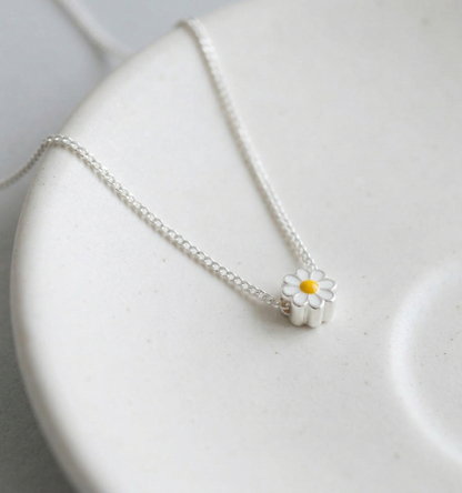 Dainty 925 sterling silver daisy flower pendant necklace with white enamel petals and yellow enamel center, displayed on a white ceramic plate