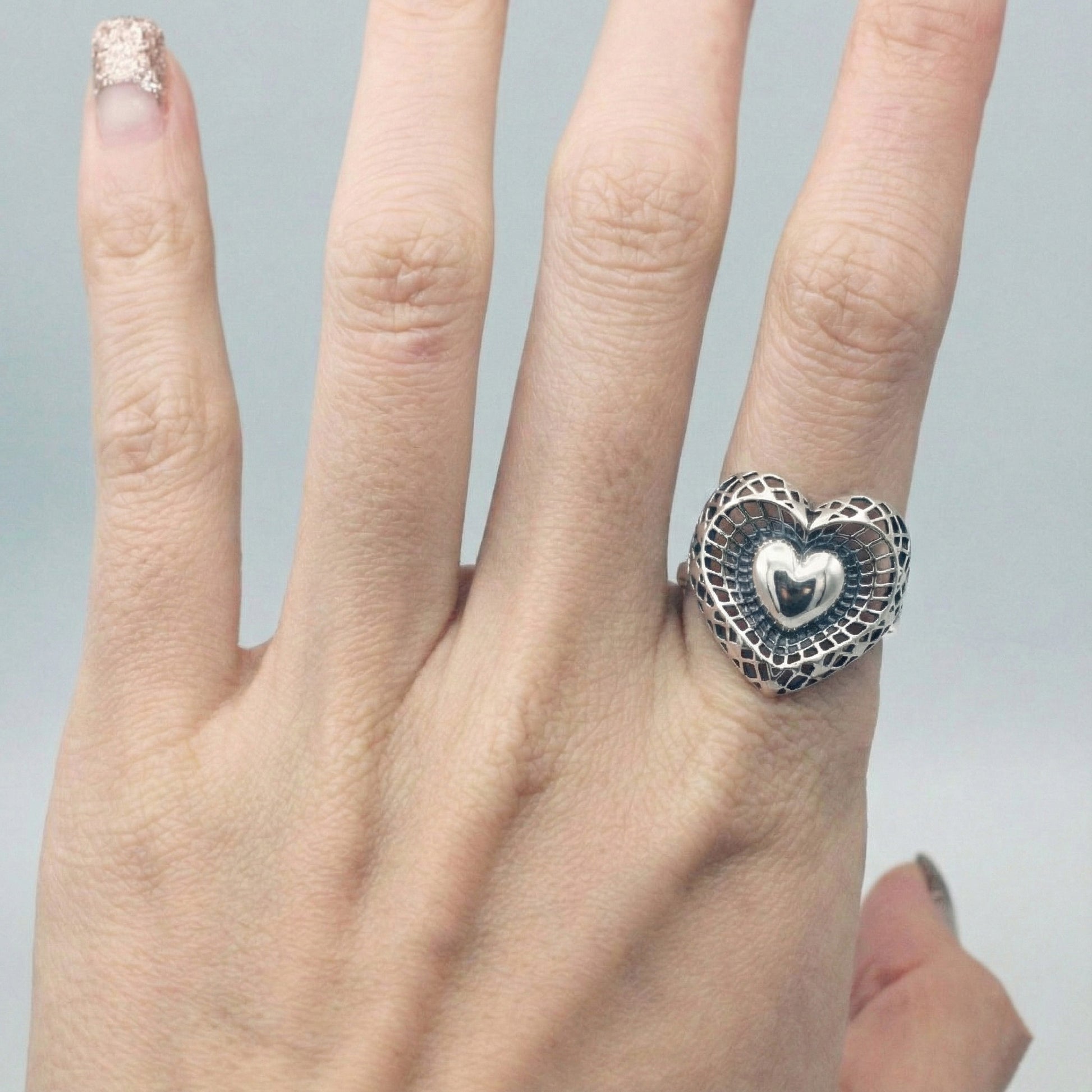 925 sterling silver filigree heart ring on middle finger showing oxidized lattice pattern and polished puffy heart