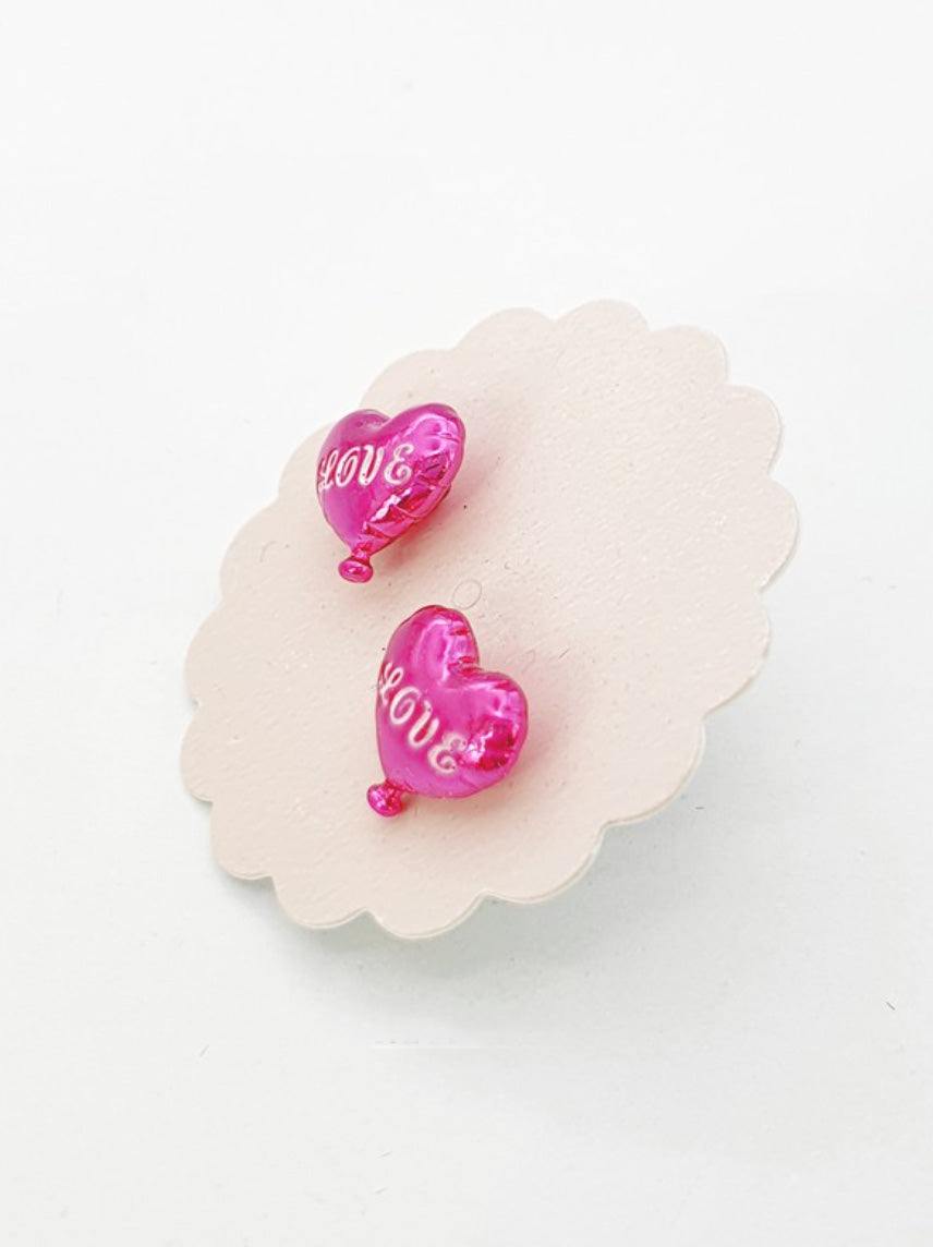 Magenta pink heart balloon earrings with LOVE engraving on white floral display pad