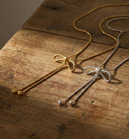 Gold and silver ribbon bow lariat necklaces on wooden display - adjustable Y-drop snake chain jewelry
