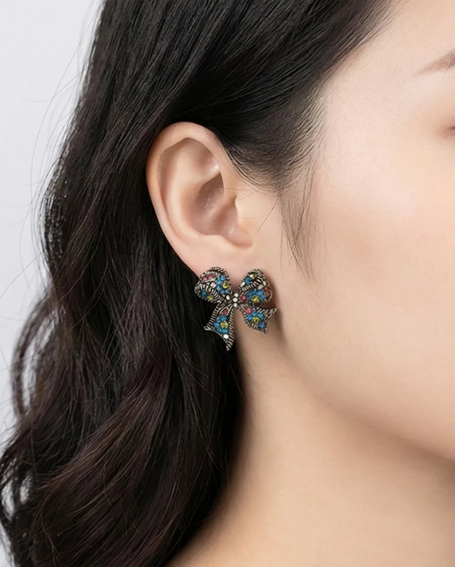 Woman wearing Silver Blue crystal bow stud earring with rhinestone and blue crystal detail — close-up ear shot, gray background, handmade in Korea