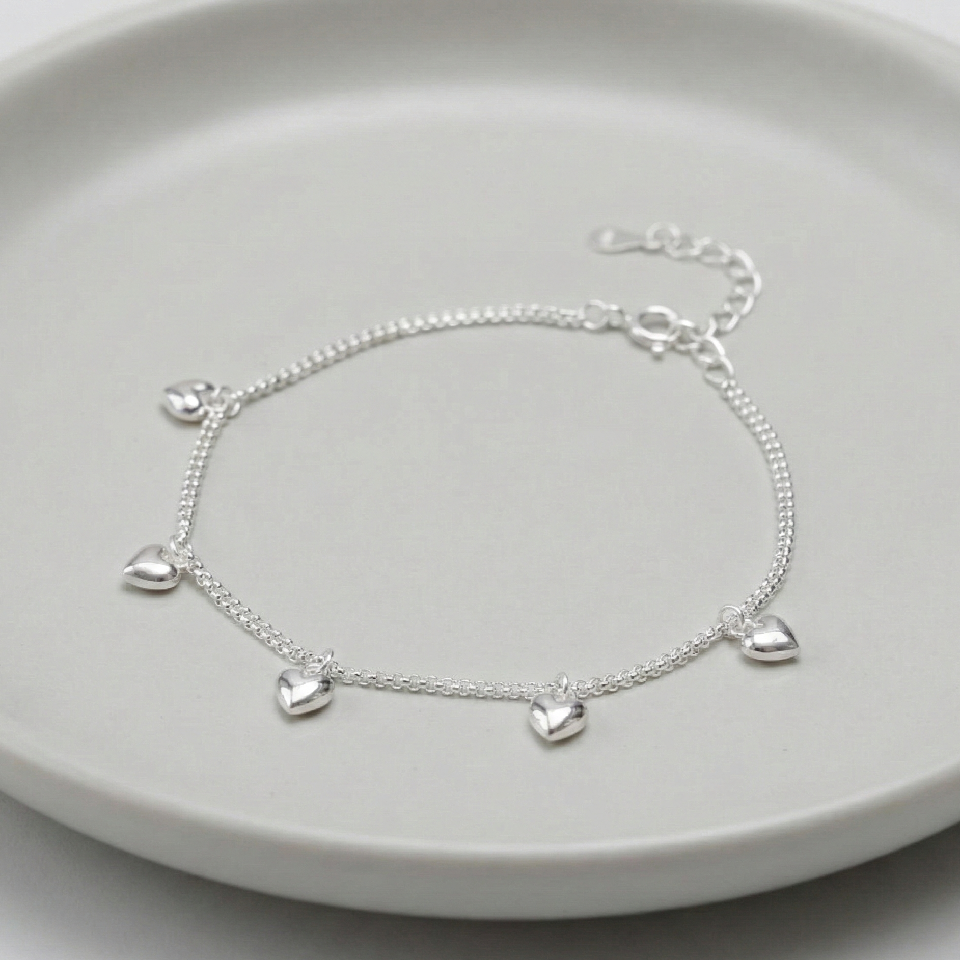 925 sterling silver double chain puffed heart charm bracelet laid on a grey ceramic plate, showing 5 dangling 3D heart charms and adjustable extender chain