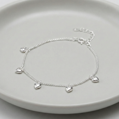 925 sterling silver double chain puffed heart charm bracelet laid on a grey ceramic plate, showing 5 dangling 3D heart charms and adjustable extender chain