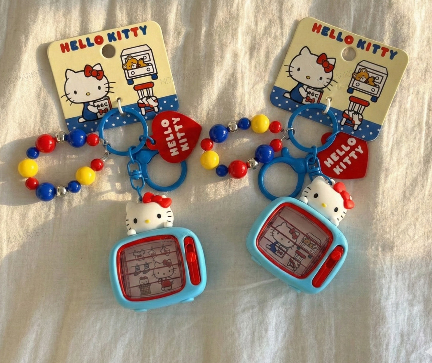 Two genuine Sanrio Hello Kitty retro TV 3D figure keychains with colorful red blue yellow bead chain and red heart charm on white fabric background