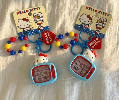 Two genuine Sanrio Hello Kitty retro TV 3D figure keychains with colorful red blue yellow bead chain and red heart charm on white fabric background