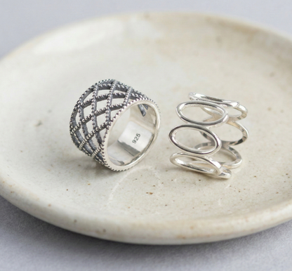 Two 925 sterling silver bold rings on a ceramic dish — vintage lace lattice wide band and modern oval loop wide band, showing 925 hallmark stamp inside