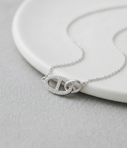 Close-up of 925 sterling silver pavé CZ interlocking double ring necklace resting on a white ceramic plate, showcasing the detailed cubic zirconia setting