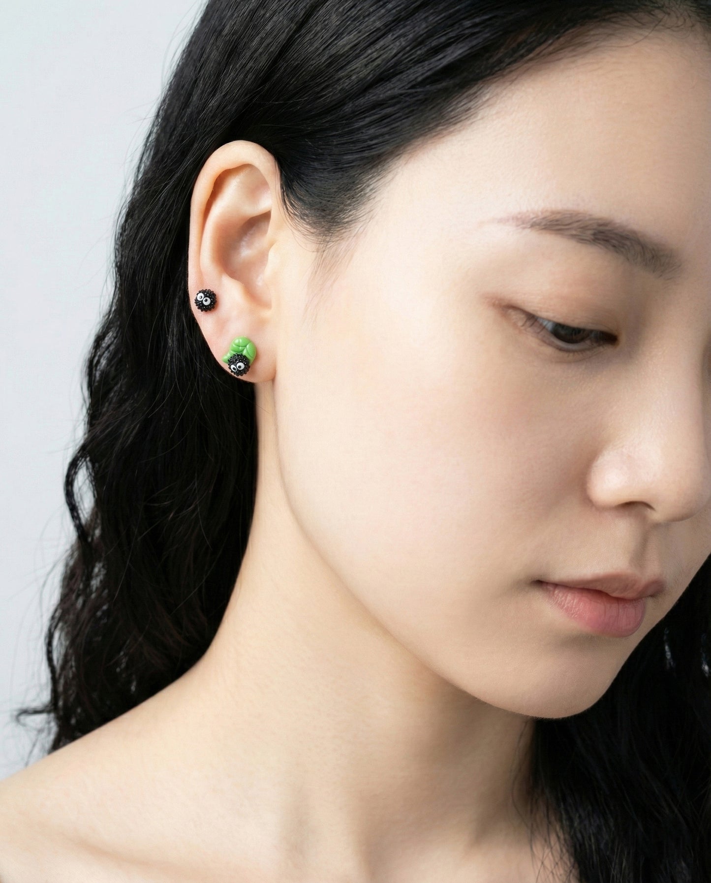 Model wearing layered Soot Sprite earrings with green leaf version and classic sprite in double piercing