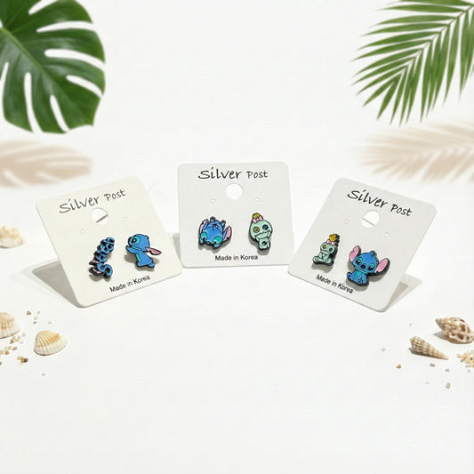 Three sets of Stitch and Scrump earrings on white display cards, silver post, playful enamel design."