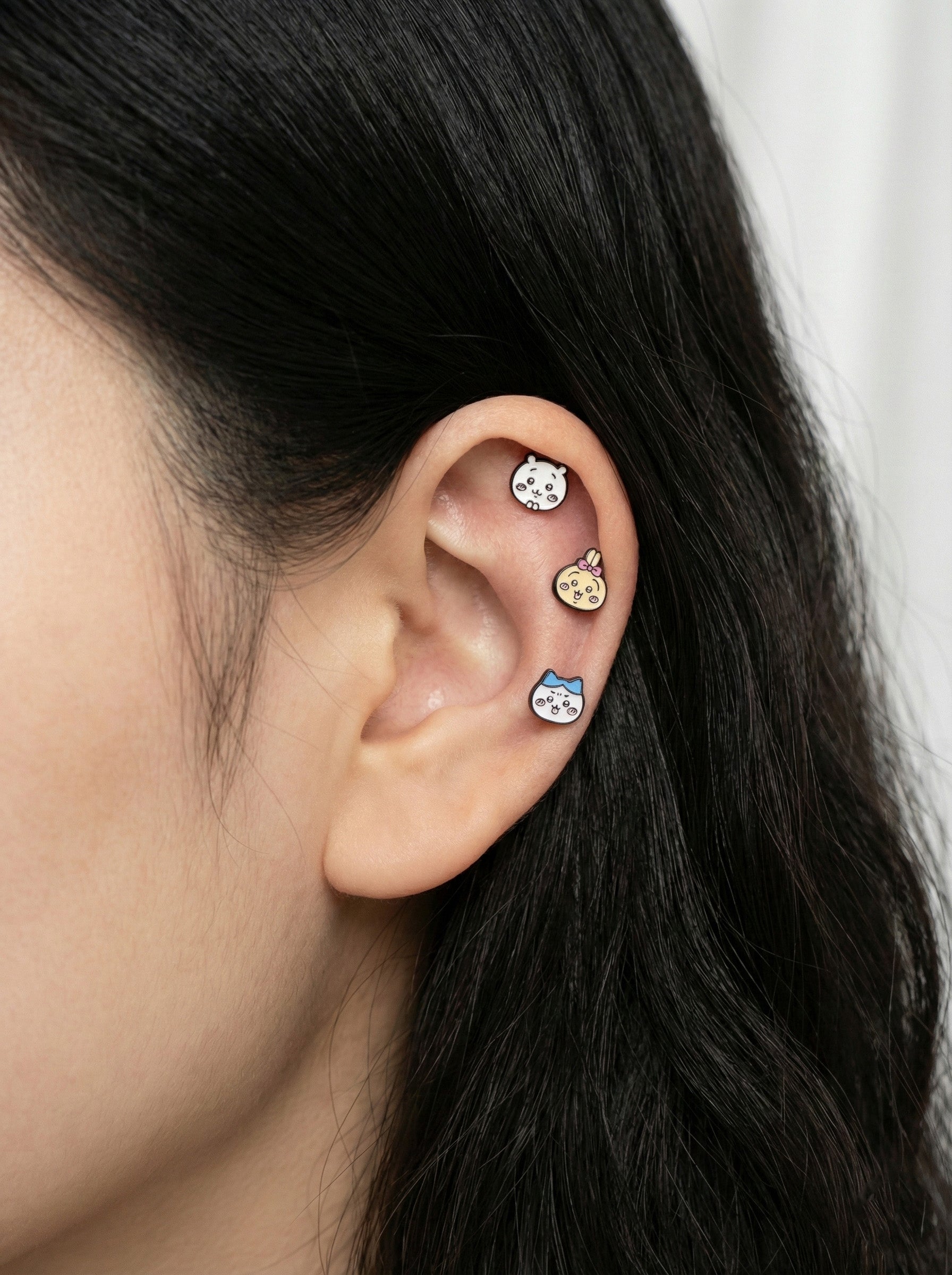 Close-up of an ear with three small earrings on a plain background