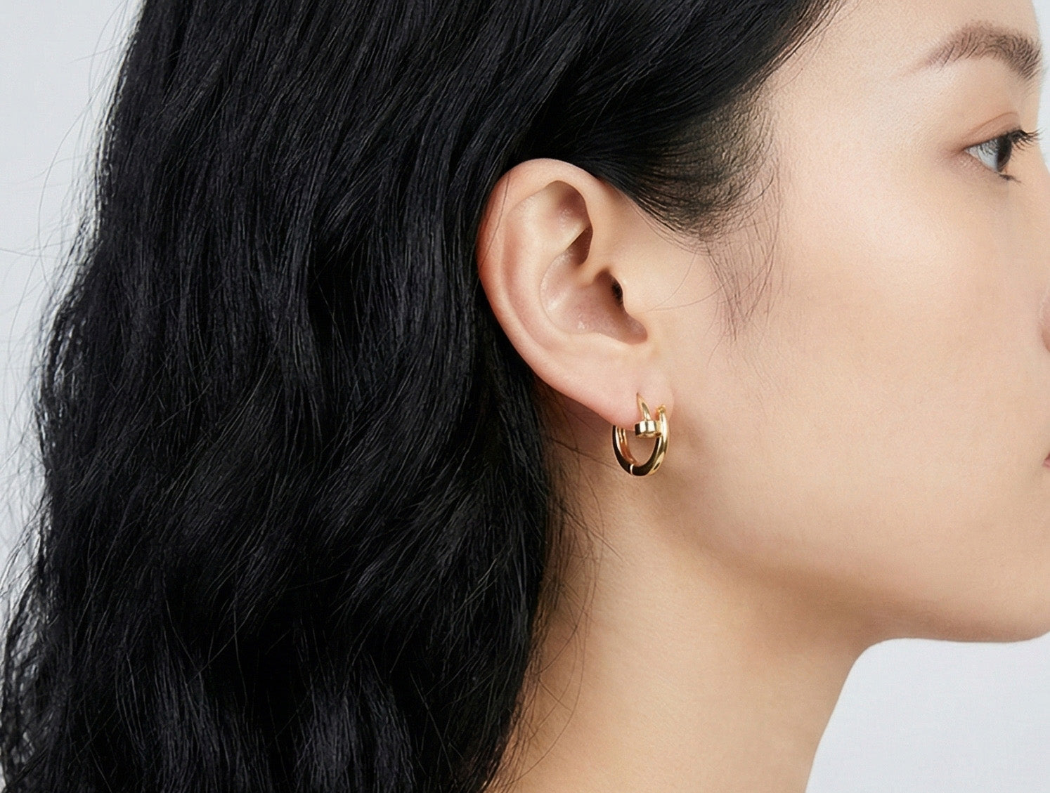 Model wearing two gold hoop earrings with modern interlocked design on lobe.