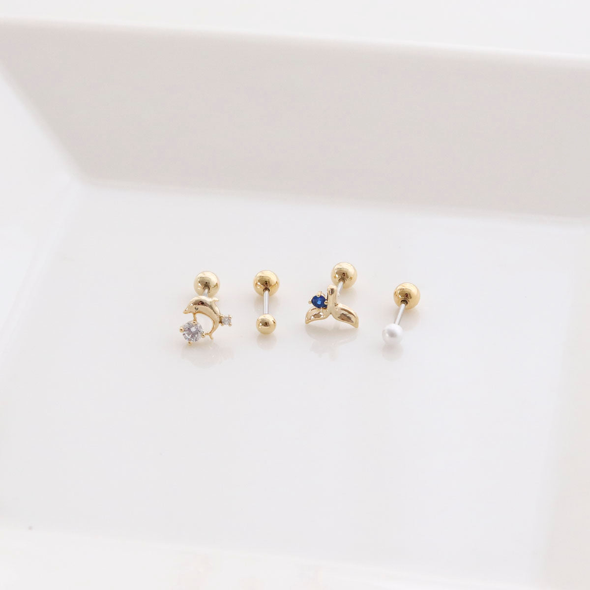 Four-piece barbell ball stud earring set featuring dolphin, whale tail, pearl and basic ball designs on white background