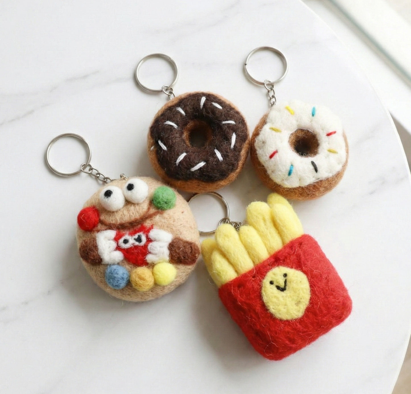 Four handmade wool felt keychains from Nepal - chocolate donut, vanilla donut, cookie monster, and happy fries bag charms