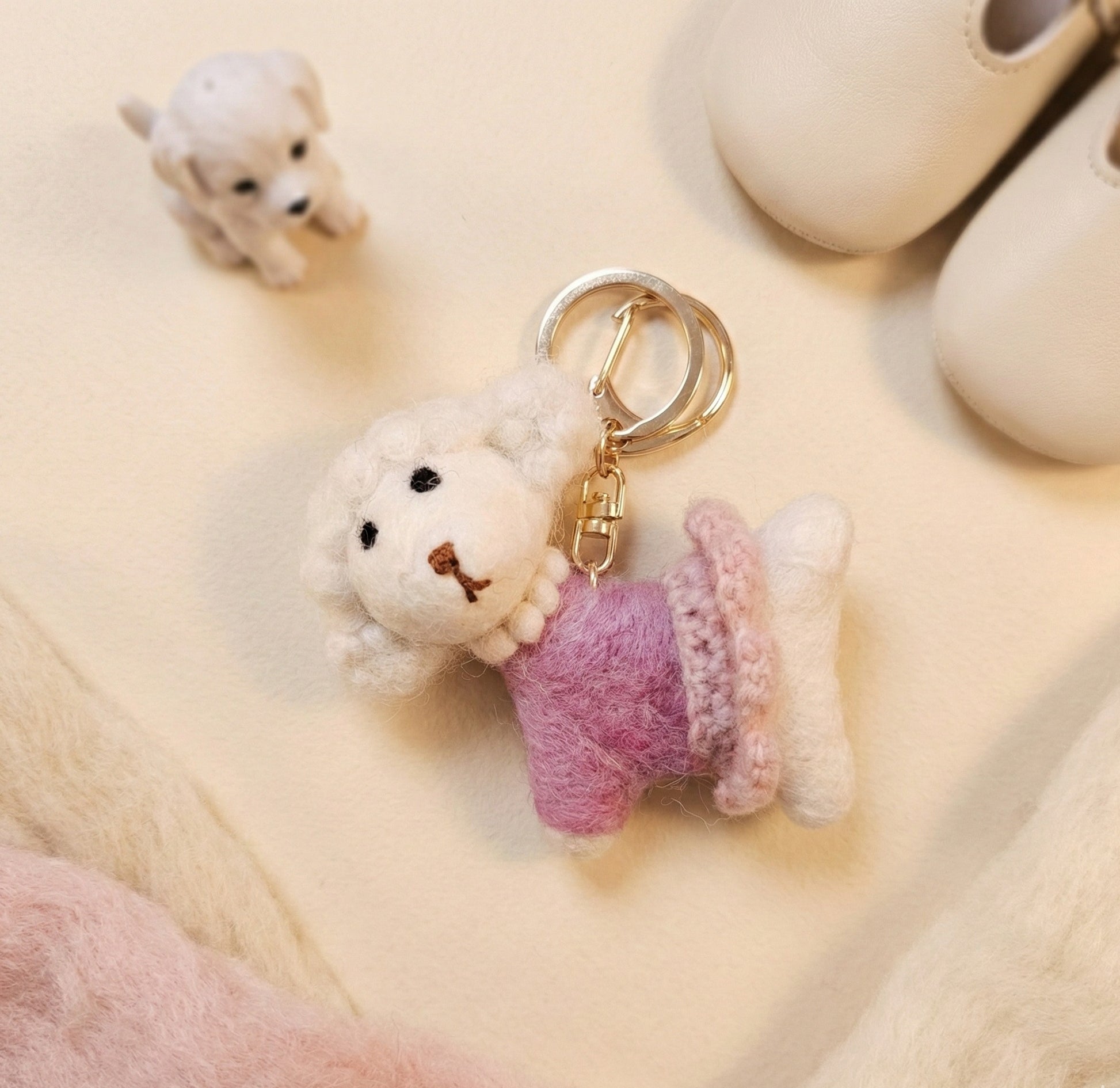 Handmade wool felt poodle keychain with pink crochet dress on beige background